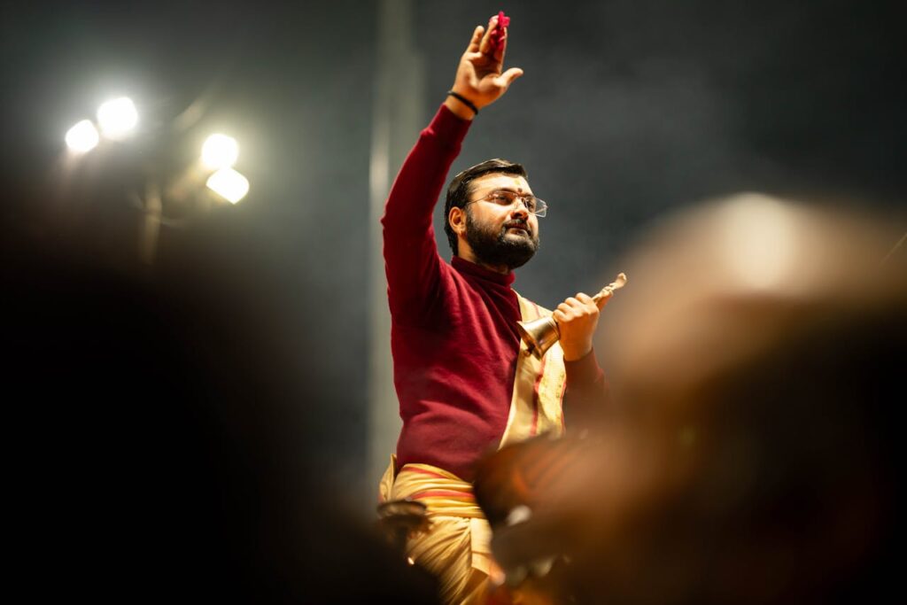 A priest in traditional attire performing a ritual at Kumbh Mela, Prayagraj, India at night.